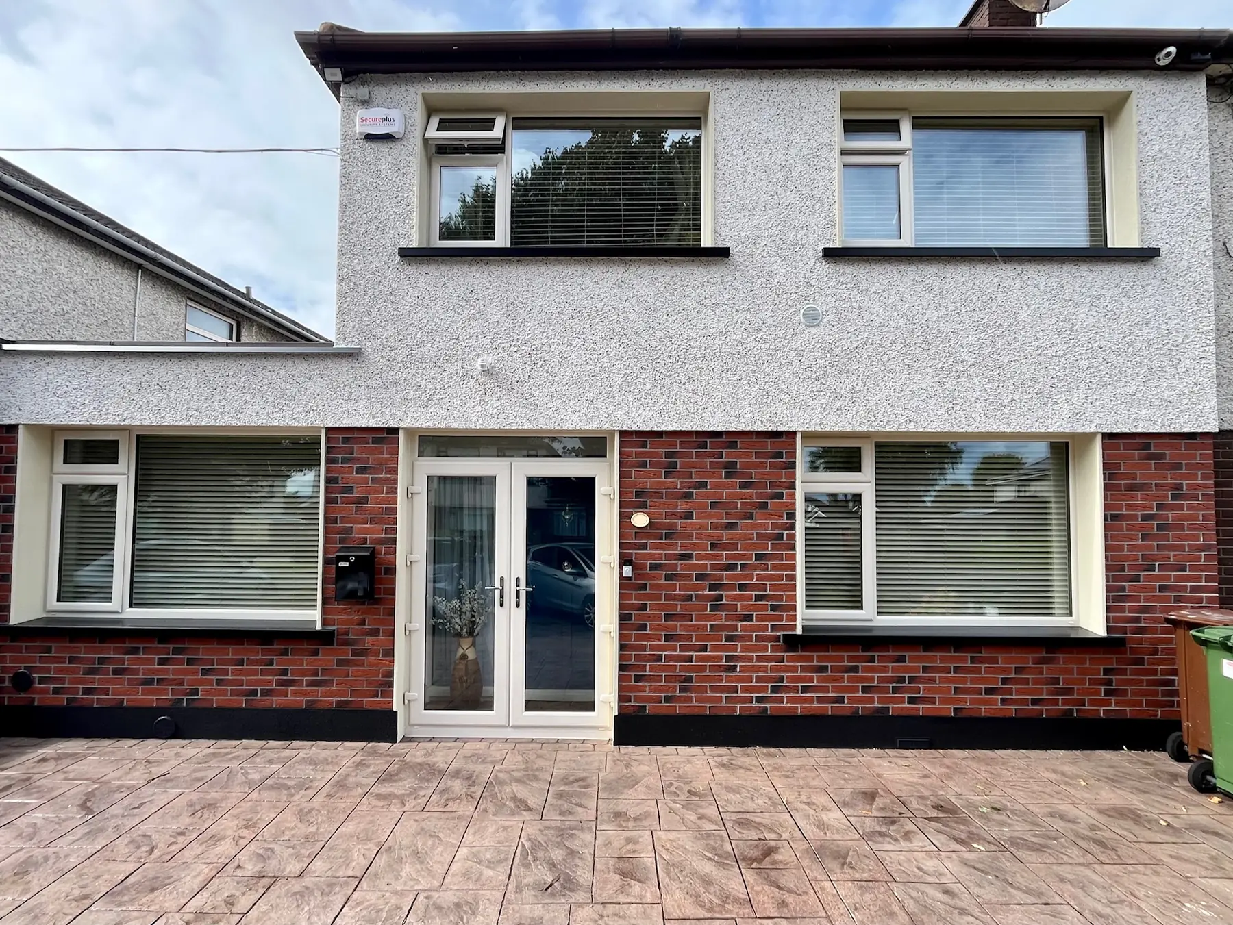 A house after external wall insulation, with a speckled render upstairs and a red brick-effect finish downstairs.