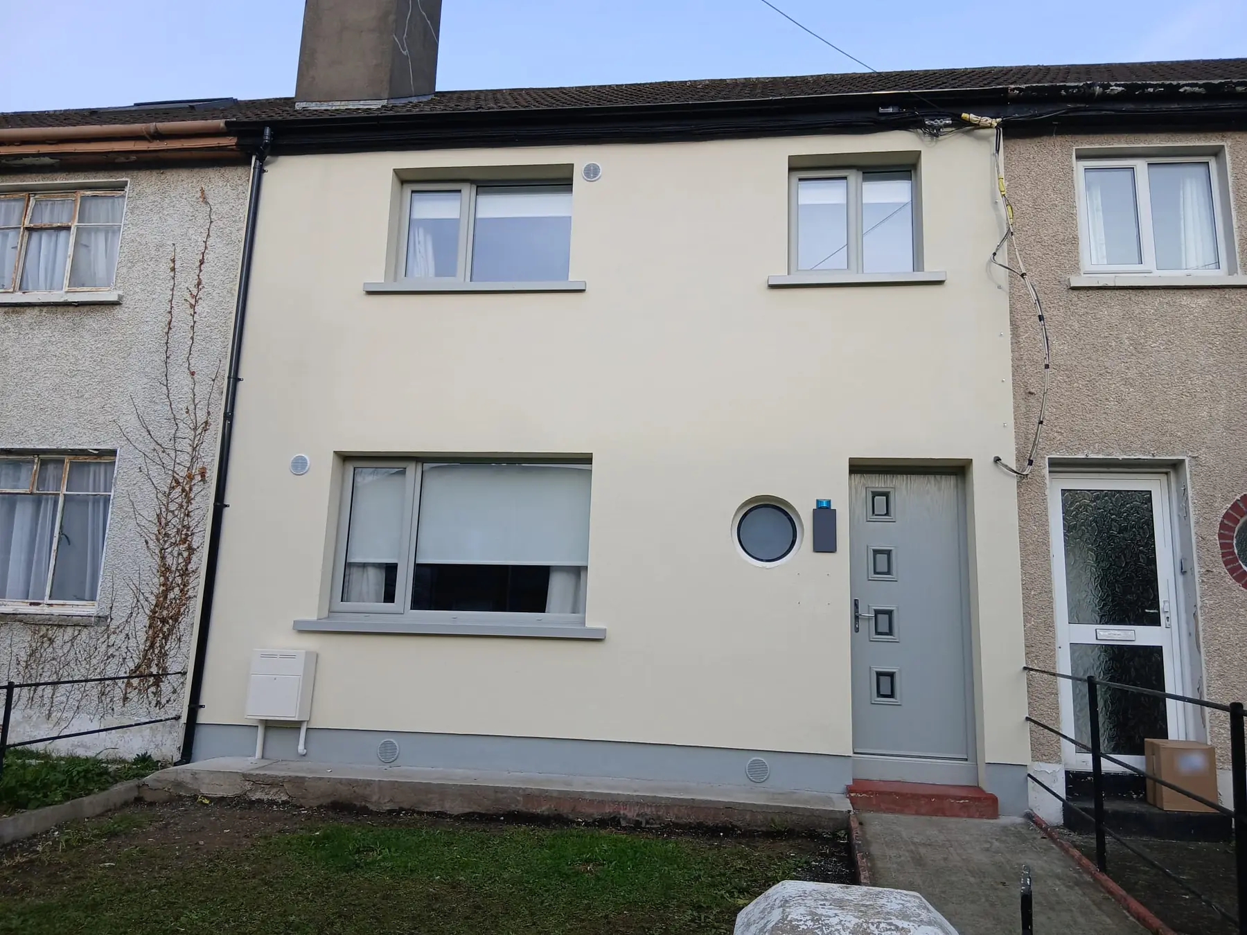A mid-terrace house after external wall insulation, with a smooth cream render finish.