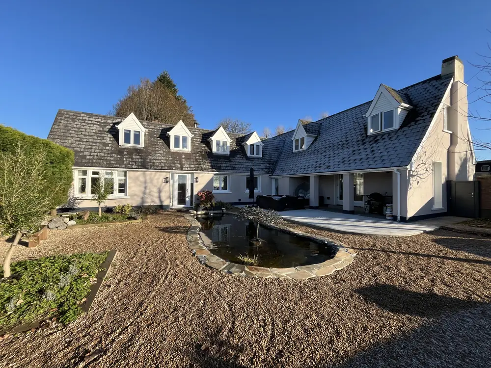 A large dormer bungalow after the job, with a smooth light render finish, a covered patio and a pond in the gravel garden.