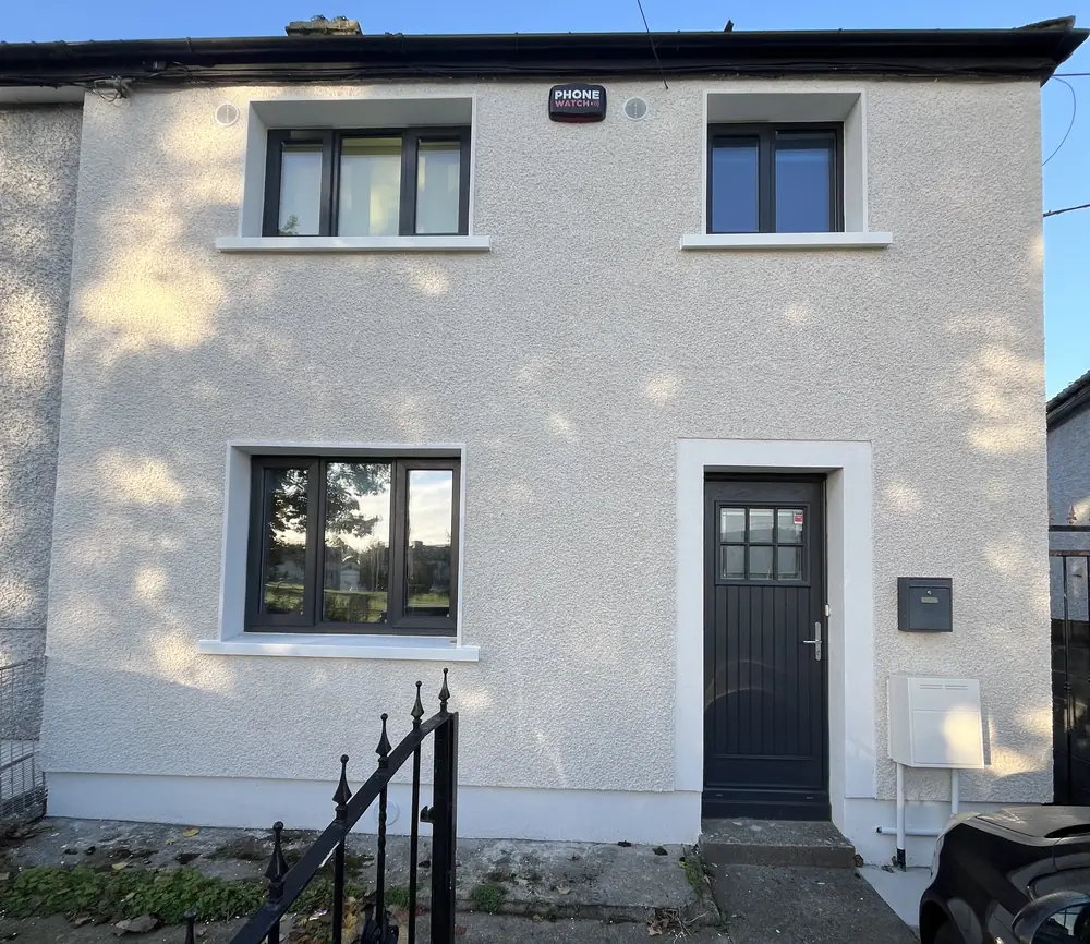 An end-of-terrace house after external wall insulation, with a light textured render finish and dark grey windows and door.