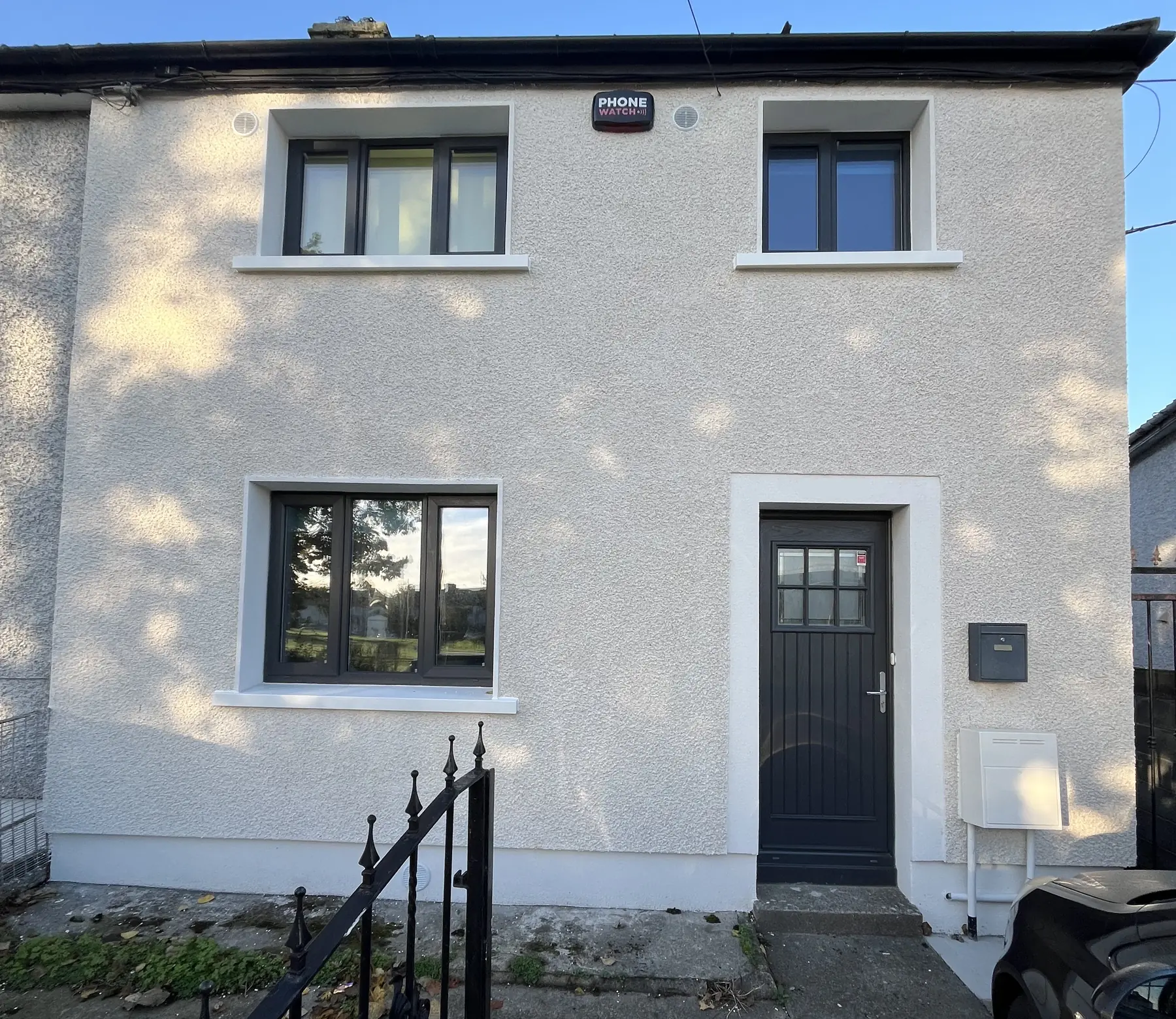An end-of-terrace house after external wall insulation, with a light textured render finish and dark grey windows and door.